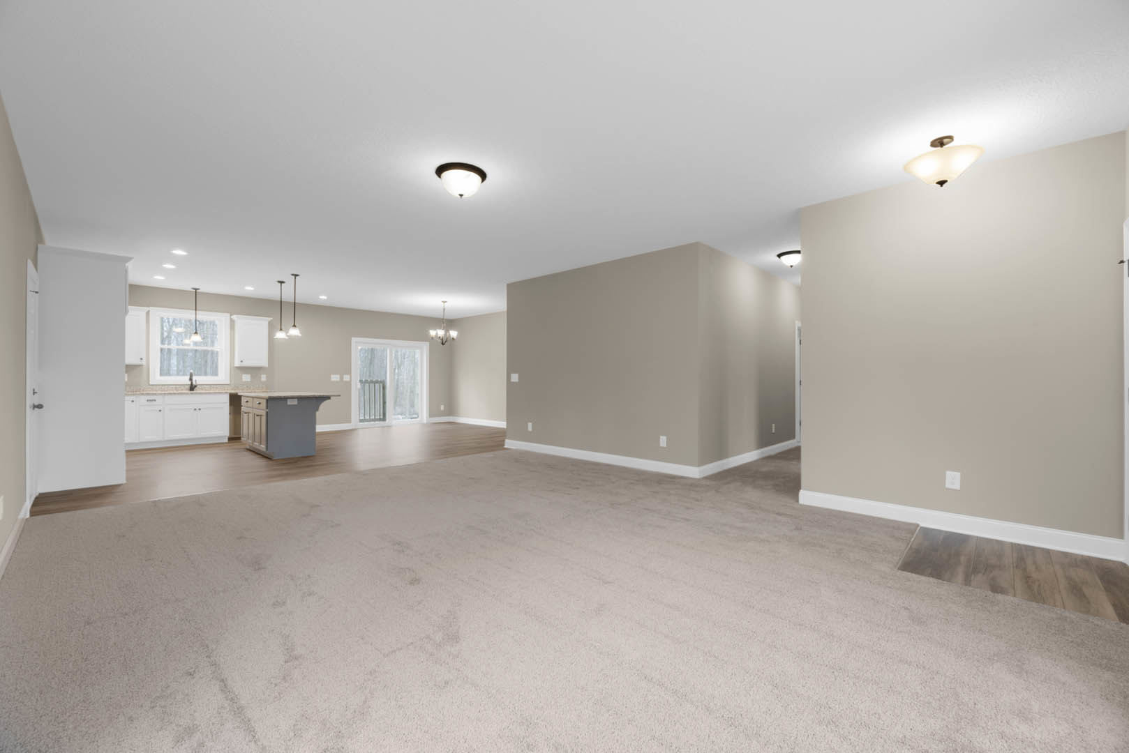 Open-concept kitchen and dining area with white cabinetry featuring black handles, wood flooring transitioning to carpet, modern ceiling light fixtures, and a white door with a