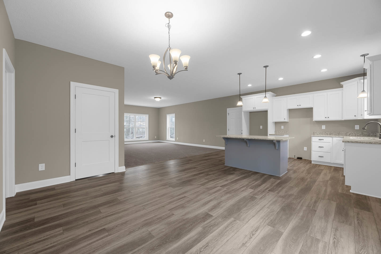Spacious kitchen with marble-topped island, hardwood flooring, white cabinetry, black door handle, modern chandelier, and large window overlooking outdoors