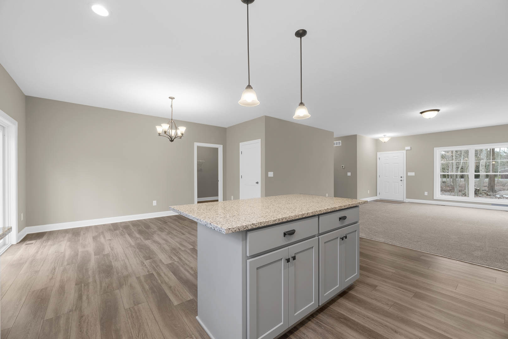 Granite kitchen island with built-in sink, white cabinetry, tile flooring, pendant ceiling lights, window overlooking trees, white door with black handle