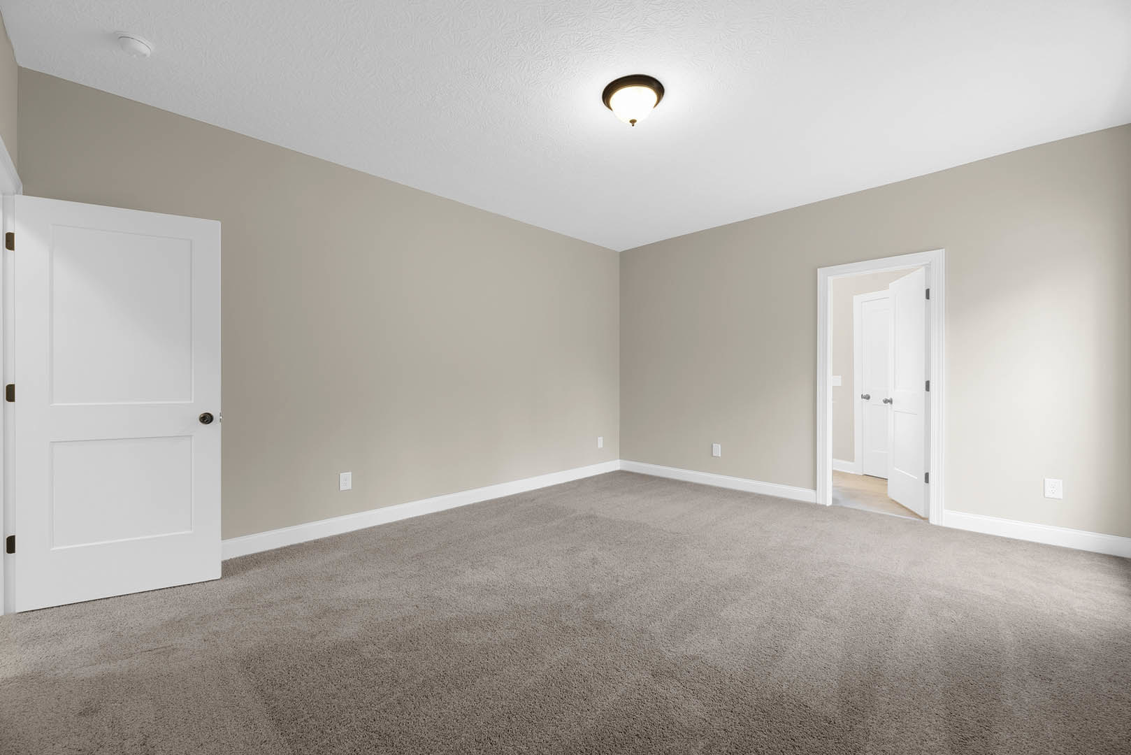 Beige walls, white paneled doors with silver knobs, white ceiling with flush light fixture, neutral carpet flooring, simple baseboard molding