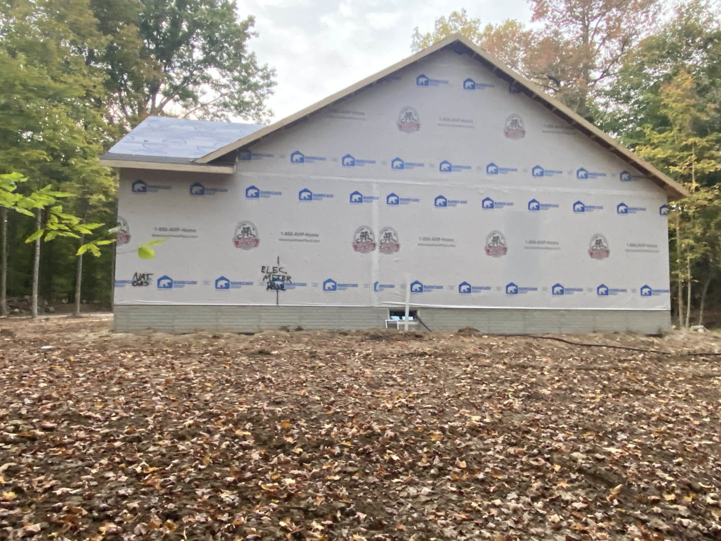 Modern home with roof covered in white insulation sheets, surrounded by trees and outdoor landscaping
