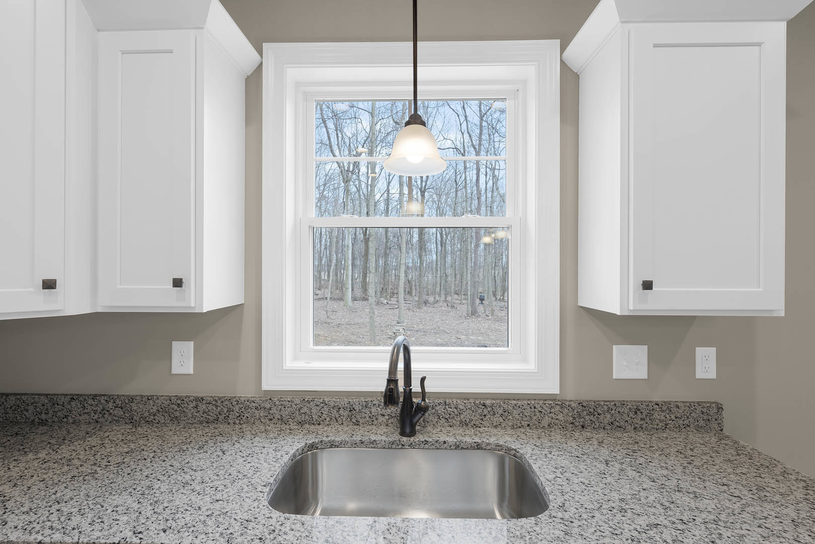 Undermount stainless steel kitchen sink with chrome faucet set in light quartz countertop, white subway tile backsplash, white cabinetry, and large window letting in natural light