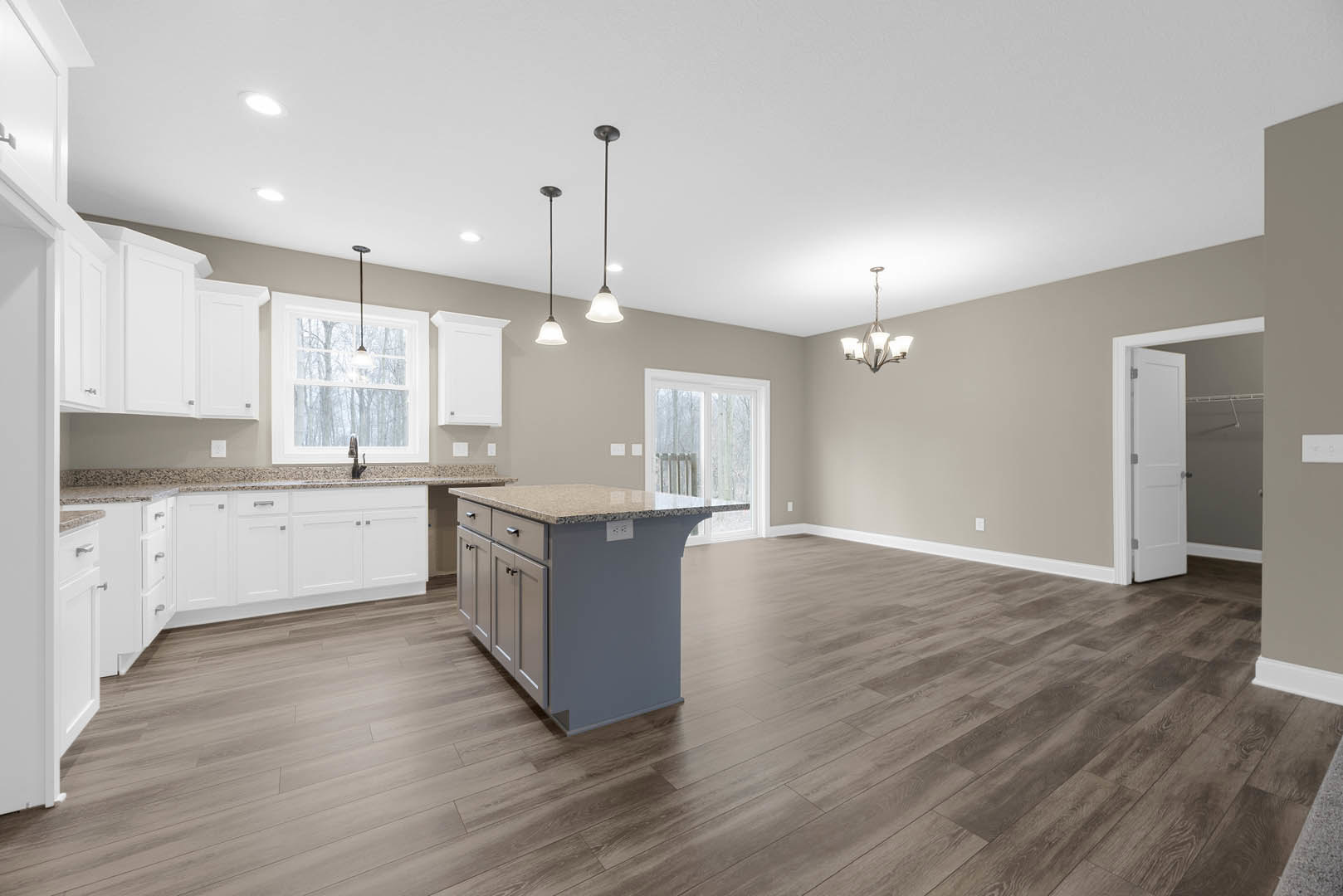 Kitchen with wood flooring, white cabinets, marble-topped island, marble countertop beneath window, stainless steel sink under pendant light, and white door with silver knobs