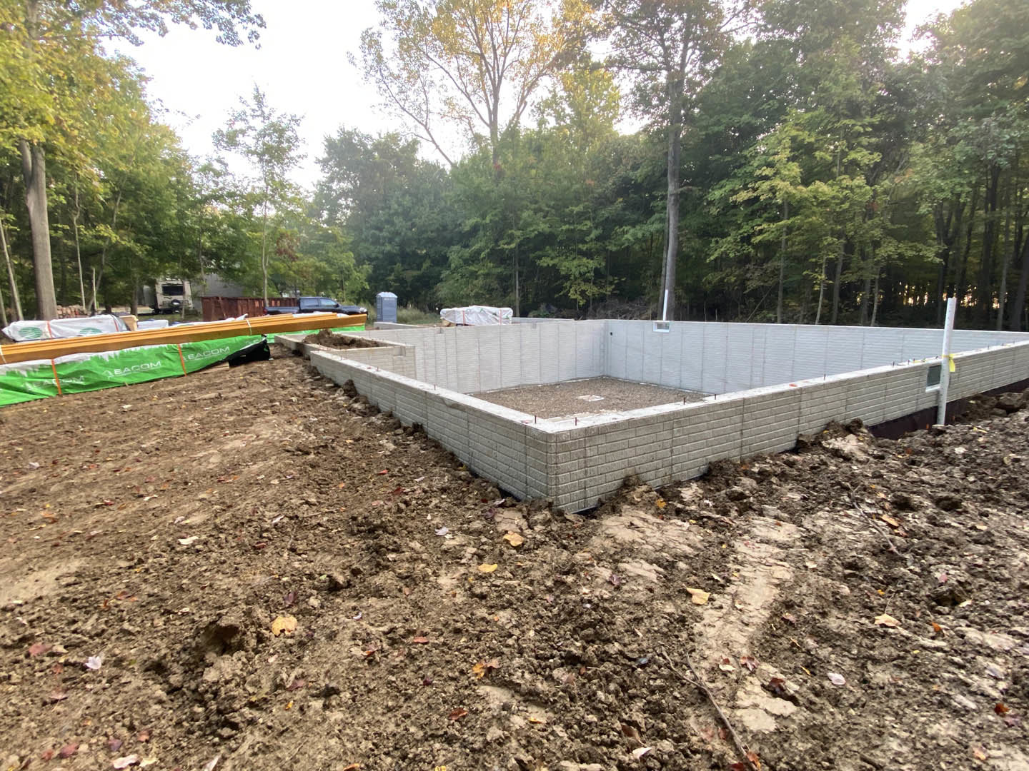 Concrete foundation with exposed dirt and green tarp, surrounded by trees and forested landscape