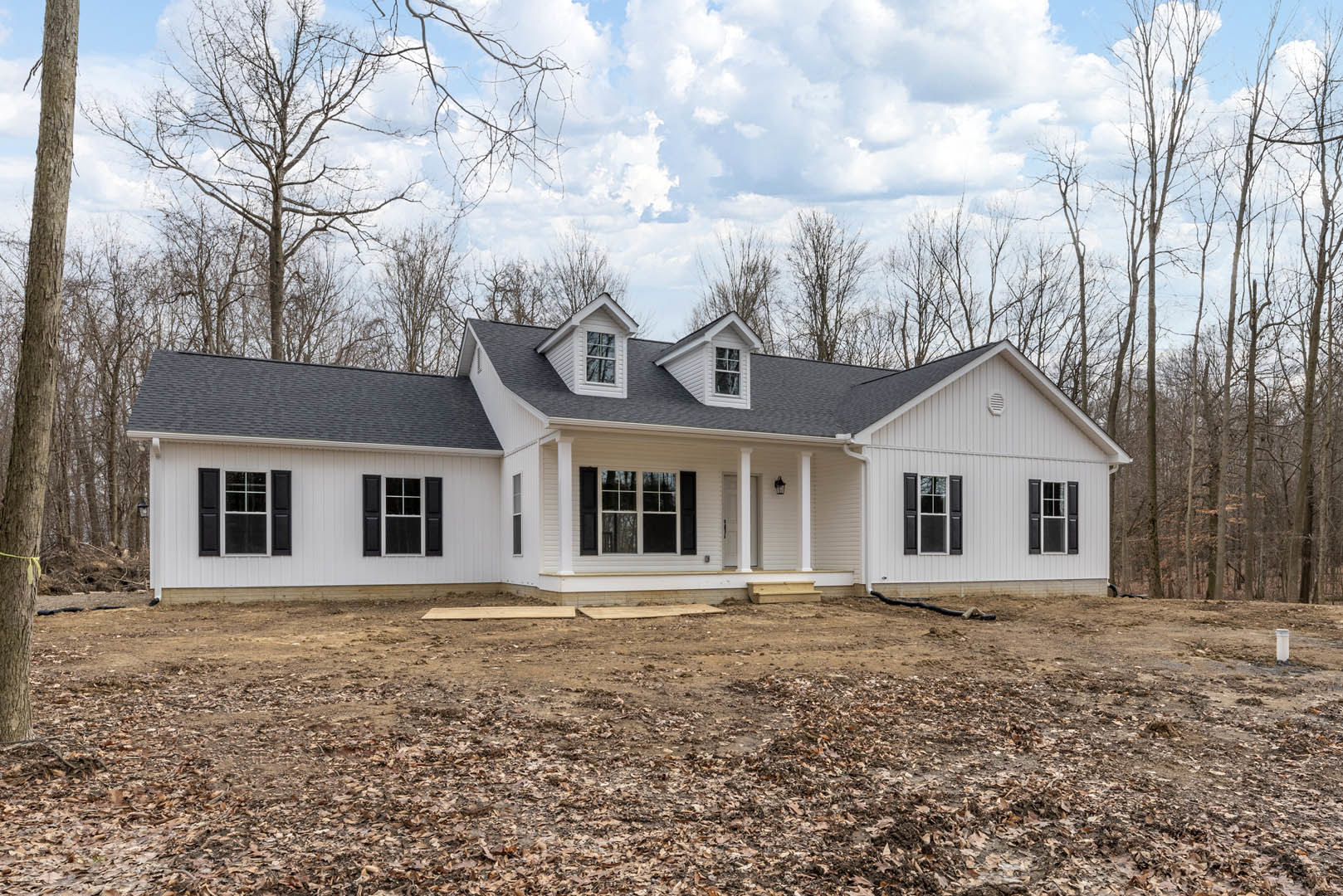 White house with black roof and white-framed windows, surrounded by leafless trees and a dirt yard scattered with leaves