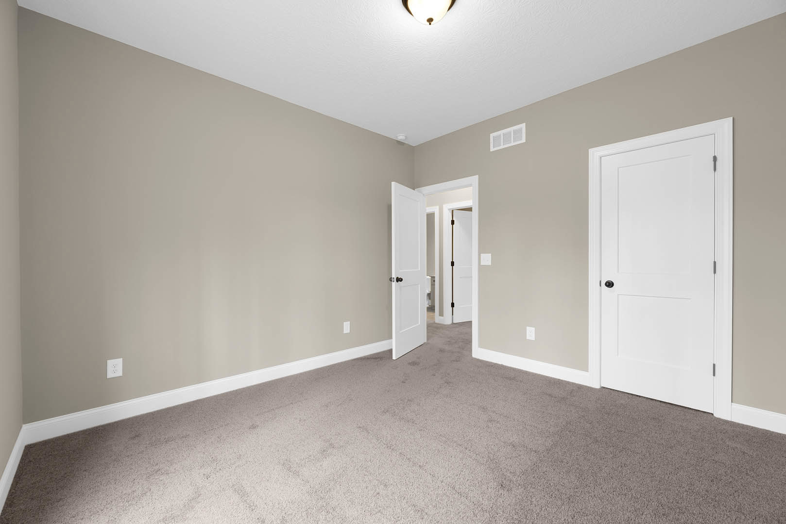 Carpeted room with two white doors featuring black knobs, wall vent, white baseboards, and smooth plaster walls