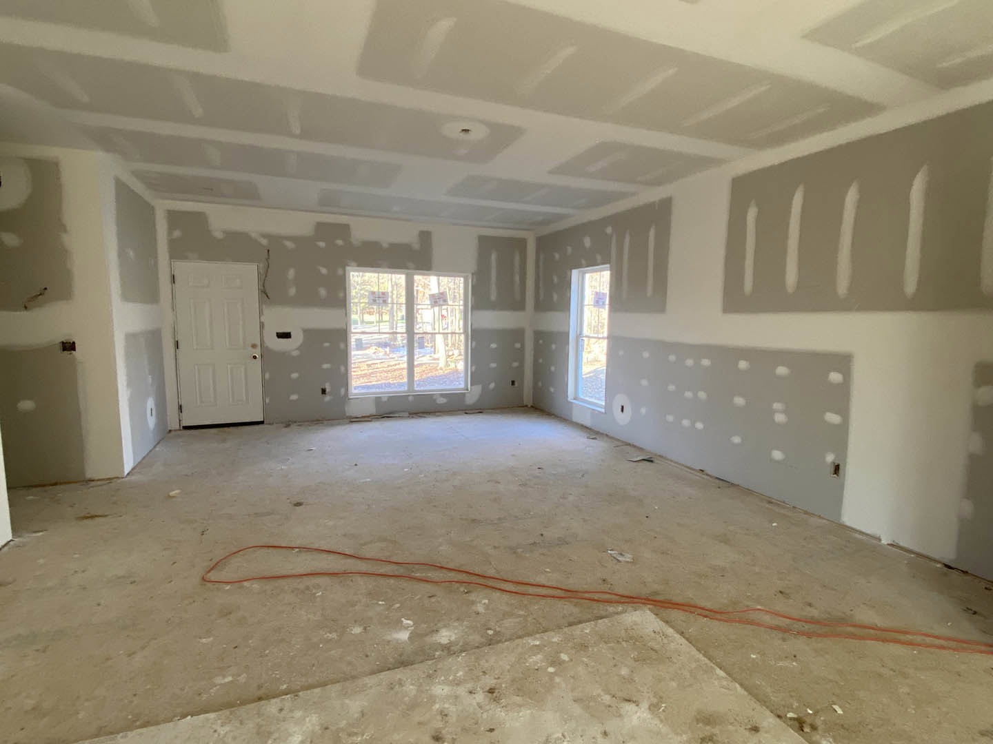 Room featuring white and gray plaster walls, white door with round knob, window with white frame displaying signs, red wire along floor, and white line marking wall.