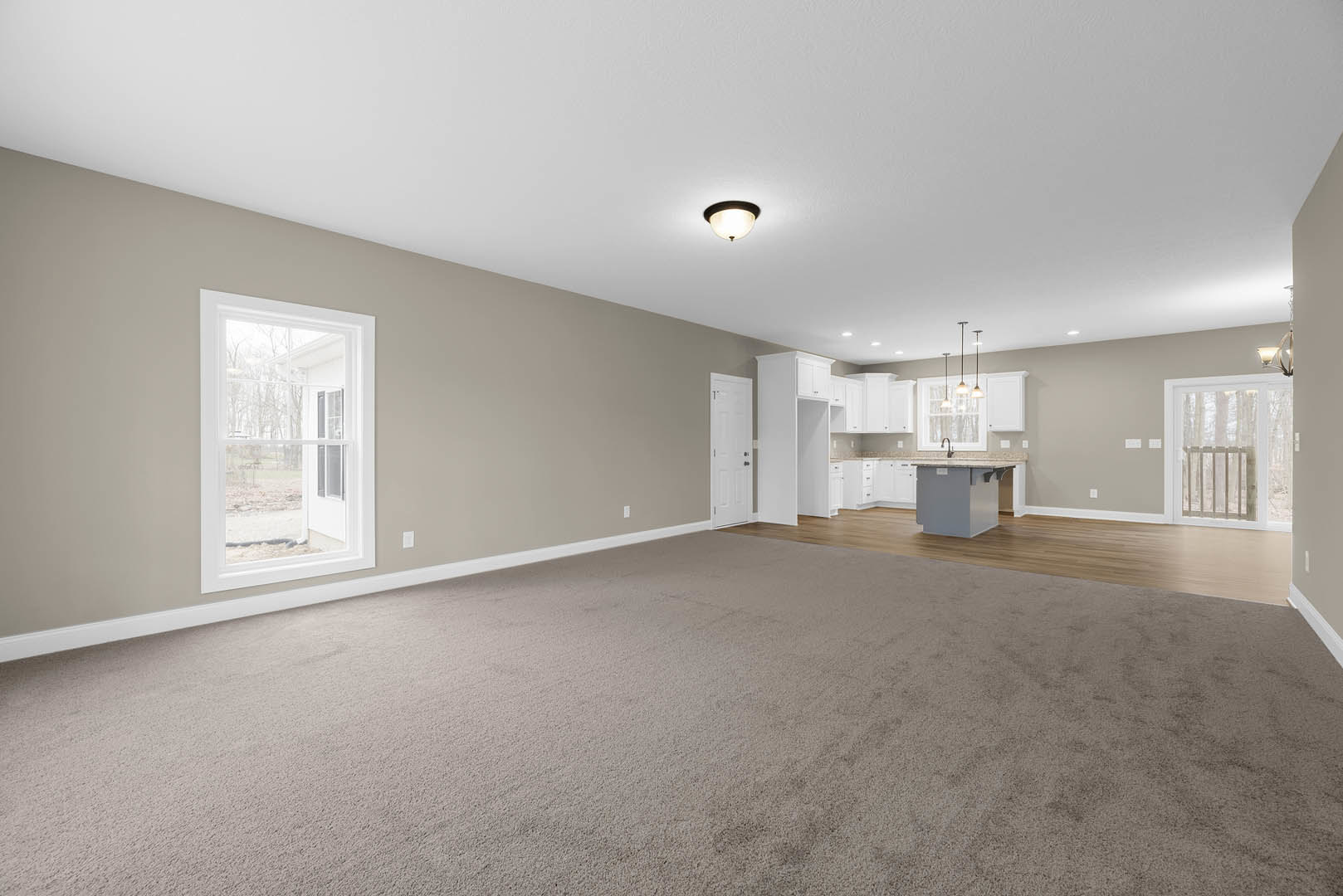 Spacious open-plan room featuring laminate flooring, white plaster walls, recessed ceiling lights, modern kitchen with cabinetry and countertops, adjacent dining area, large