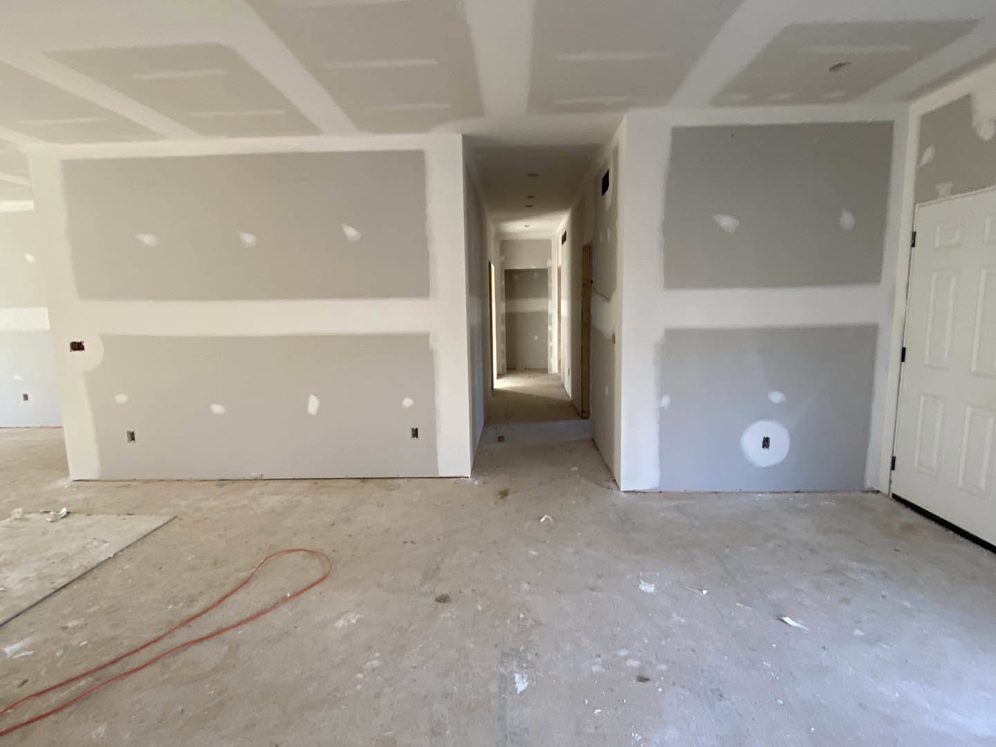 White-walled room with unfinished ceiling, visible holes, white door, and red electrical wire running along plaster surface