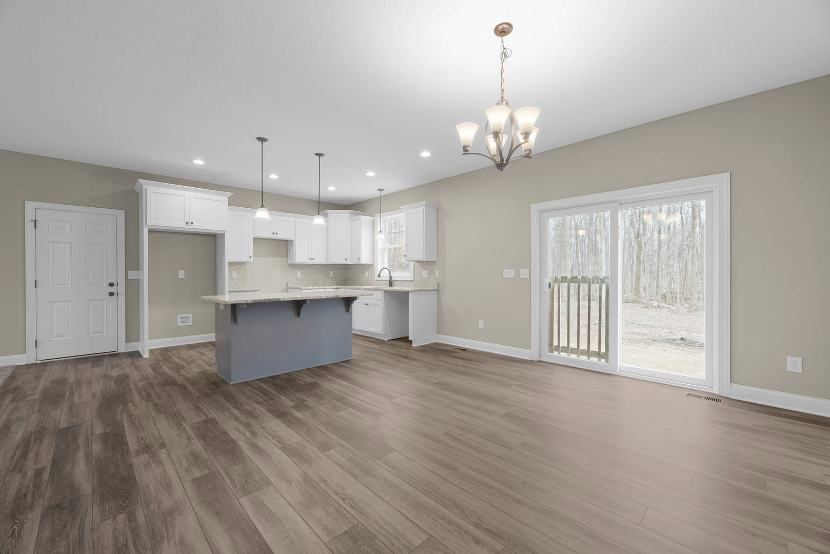Open kitchen and dining area featuring wood flooring, white cabinetry, black hardware on doors, sliding glass door overlooking wooded landscape, stone countertop, and modern