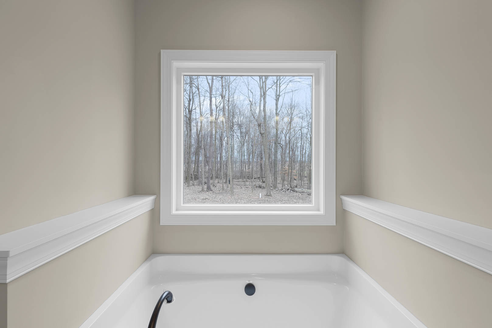 White plaster bathroom with large window overlooking trees, freestanding white bathtub, black shower head, and minimalist wall shelf.