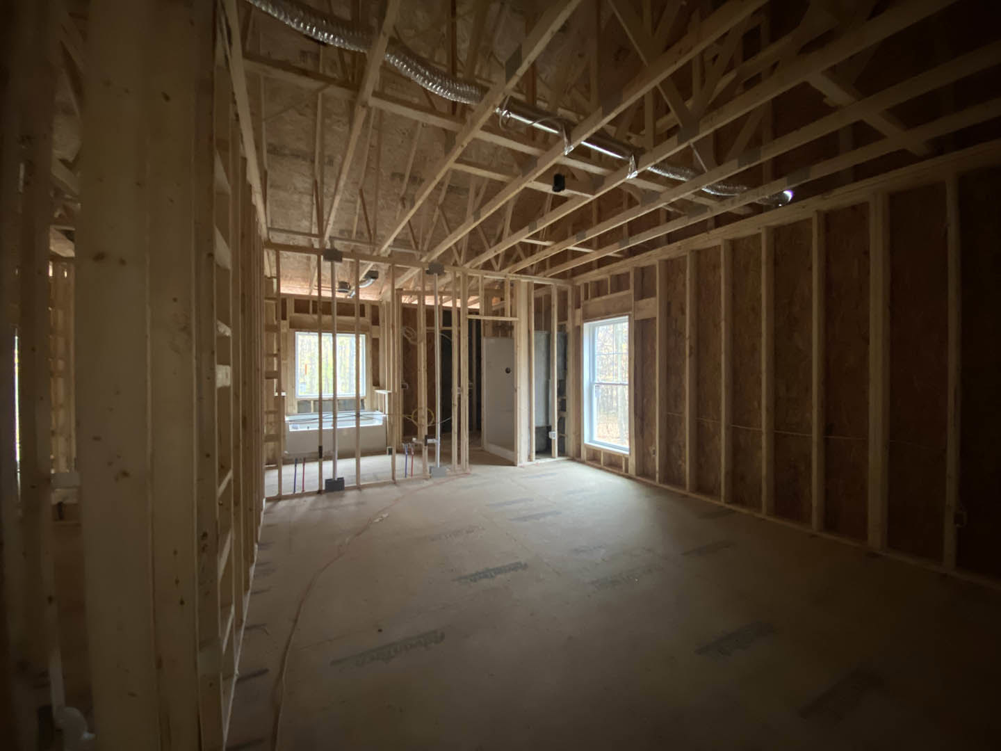 Living room with exposed wood ceiling beams, white-framed window, plaster walls, and visible metal pipes along a wood frame.