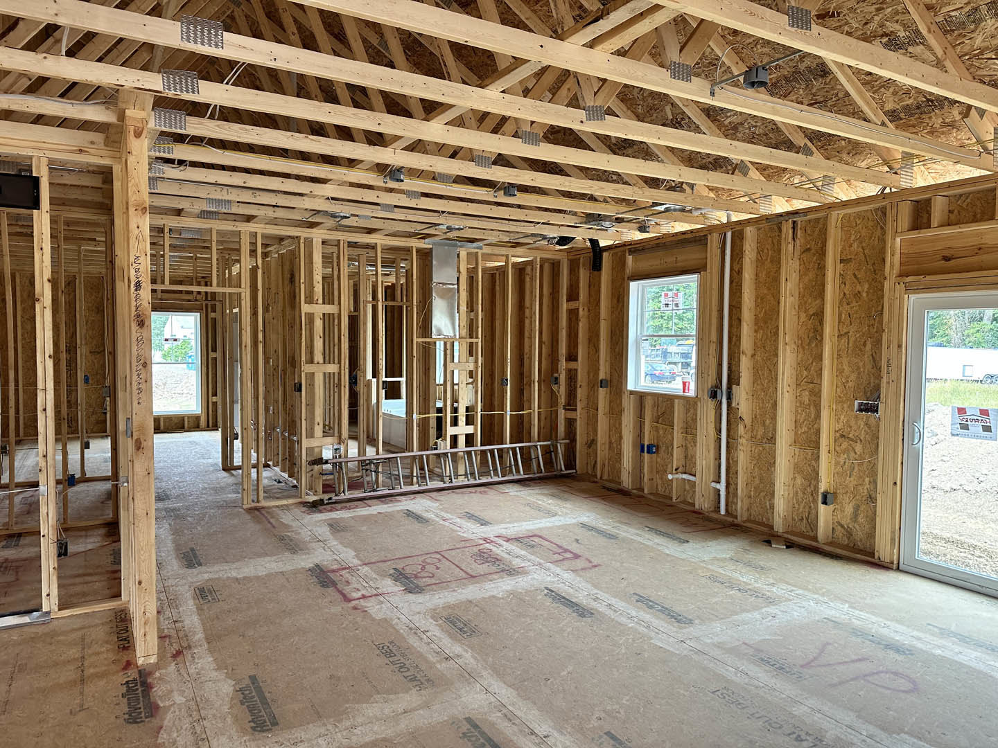 Open room with exposed wood ceiling beams, a metal ladder leaning against the wall, large window with a sign, unfinished floor, and a black screen resting on a shelf.