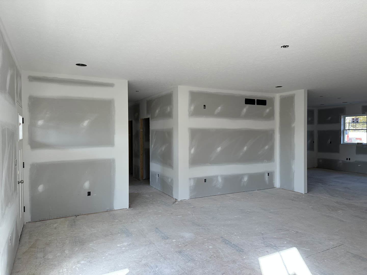 White-walled room with white ceiling, gray accent wall, window featuring a sign, light-colored flooring, and white rectangular vent cover on the wall.