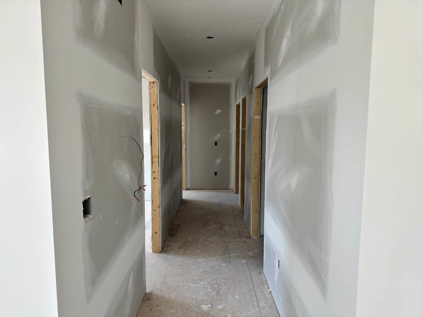 Hallway with white plaster walls, wood trim, black electrical outlet, exposed red wire, and light-colored flooring