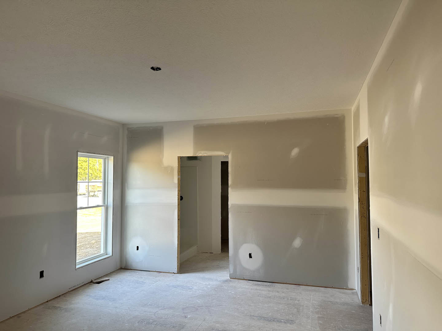 White-walled room with a concrete floor, doorway, and door; window offers street view, plaster ceiling and walls, minimal fixtures