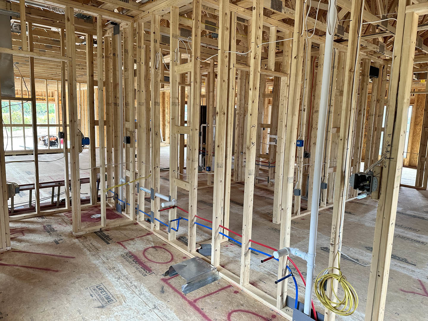 Exposed wood framing and beams inside a house under construction, with coiled electrical wire and metal hardware visible on unfinished surfaces