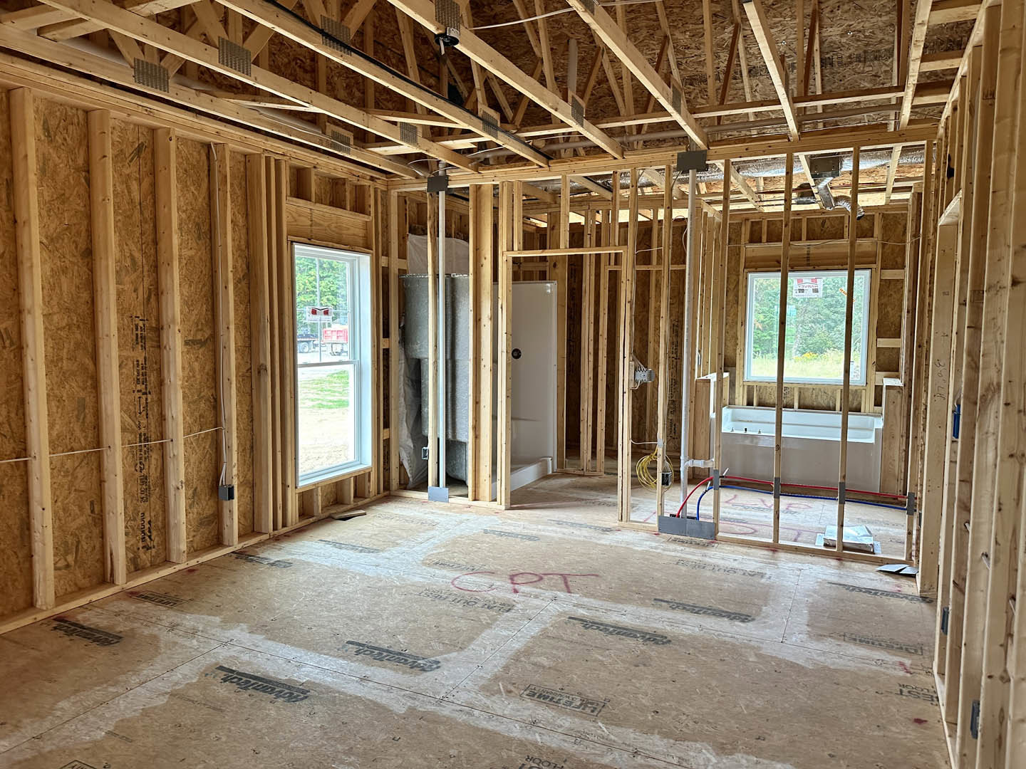 Living space with exposed wood ceiling beams, large window, hardwood flooring, and freestanding bathtub