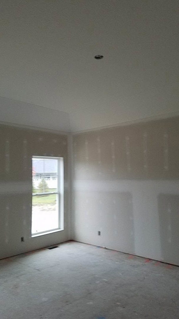 Bright room with two large windows, white plaster walls, concrete flooring, black trim, and sunlight streaming across the floor.