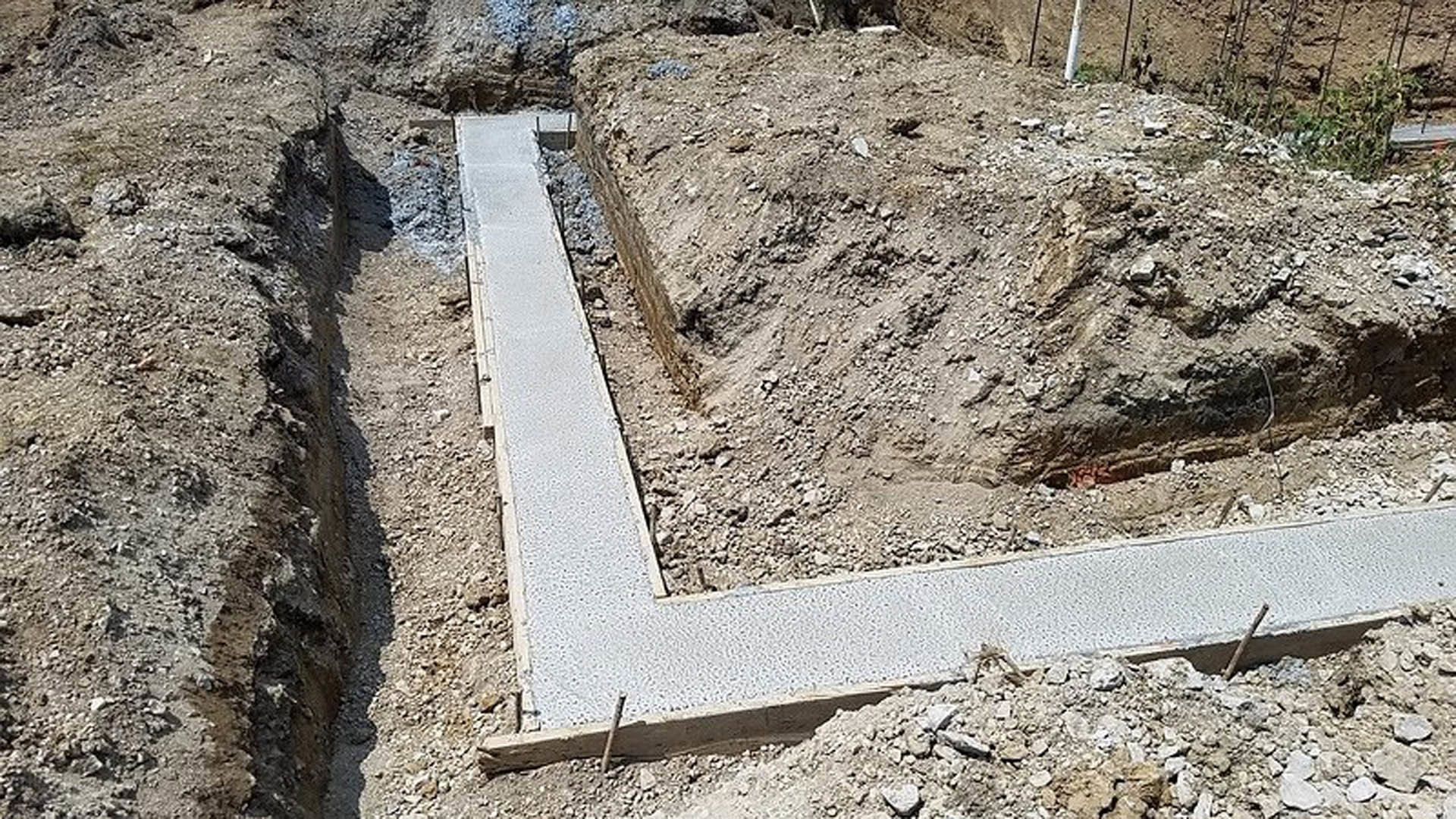 Concrete walkway bordered by loose dirt and rocks in an unfinished outdoor area