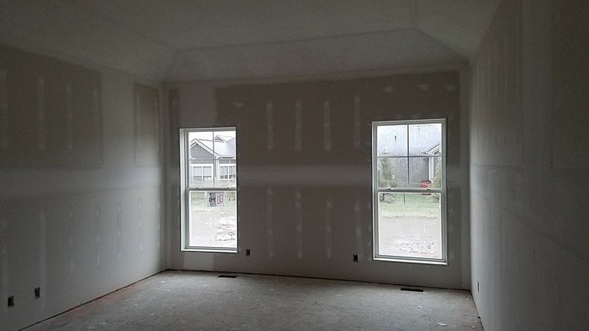 Bright room with two large windows, white plaster walls, light wood flooring, and a simple door.
