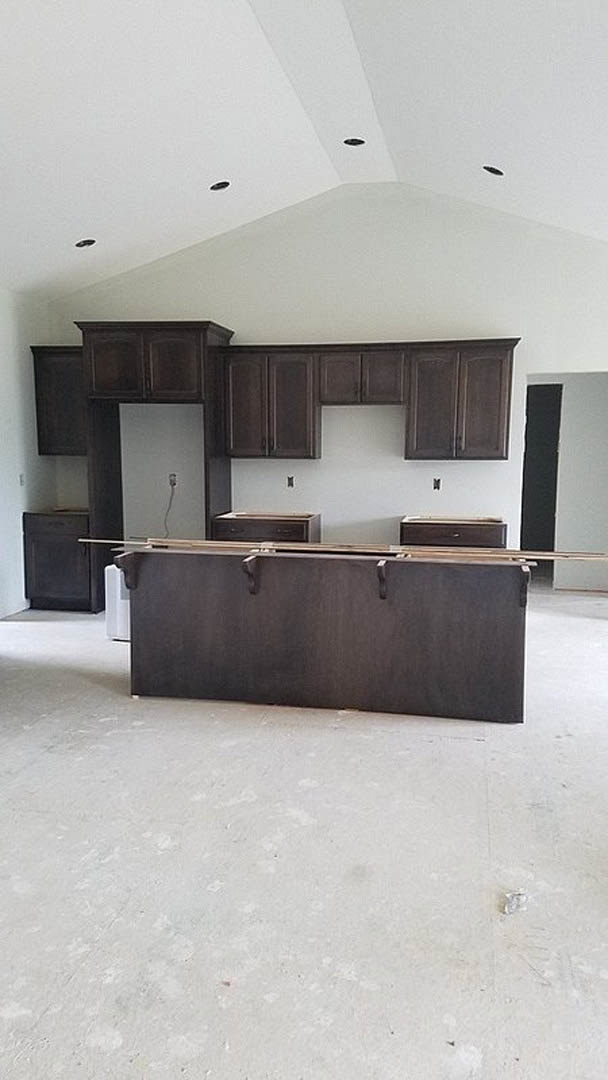 Kitchen with dark wood cabinets, light stone countertops, stainless steel sink, and black hanging pot rack with hooks above central island