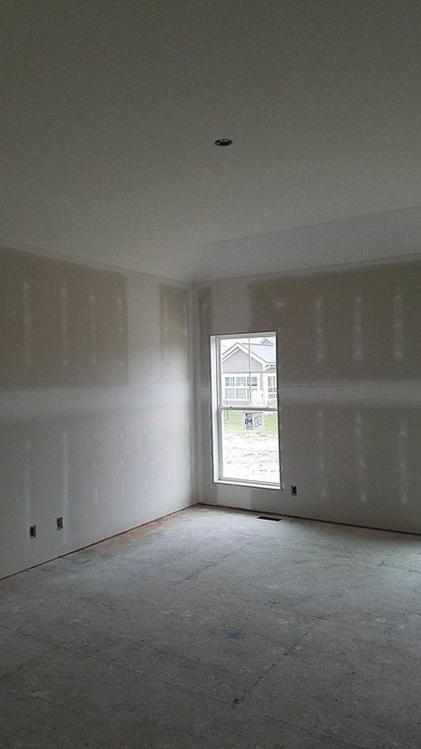 Unfinished room with plaster walls, two windows, exposed concrete floor, and visible hole in the wall
