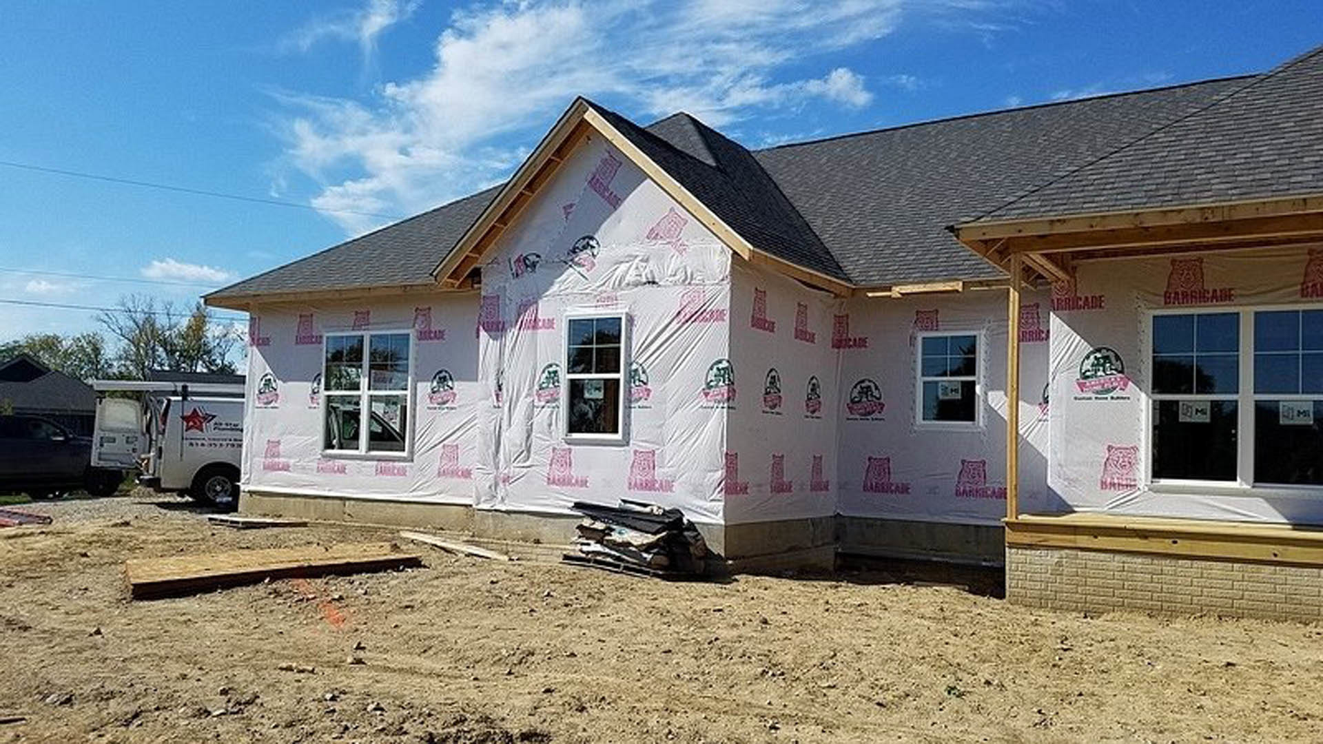 Two-story house under construction with plastic sheeting covering windows, white van parked in driveway, cloudy sky overhead