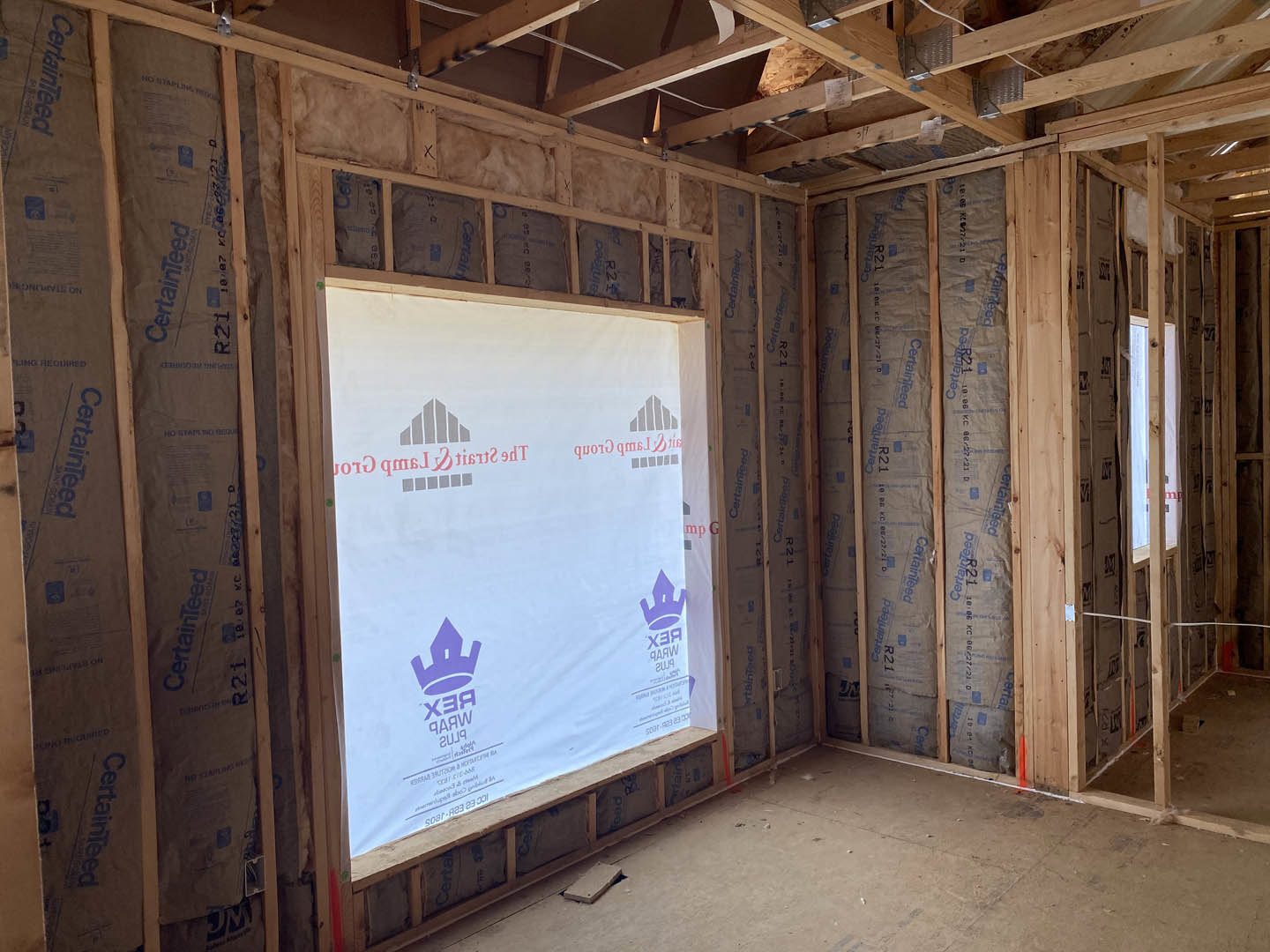Room with exposed wooden ceiling beams, white walls, large window with wood trim, and natural light illuminating the interior.