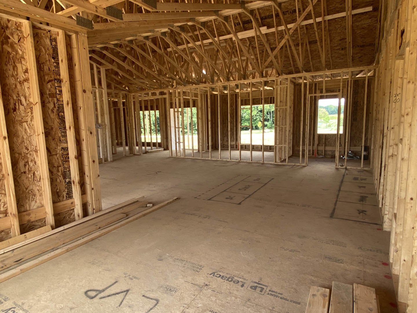 Exposed wood ceiling beams, unfinished walls, large window, subfloor with construction markings