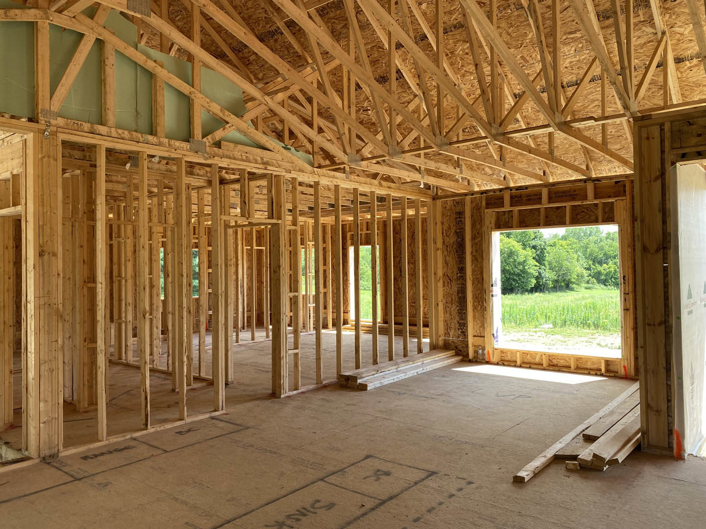 Framed window with forest view, exposed wooden beams and roof truss, unfinished floor with stacked lumber