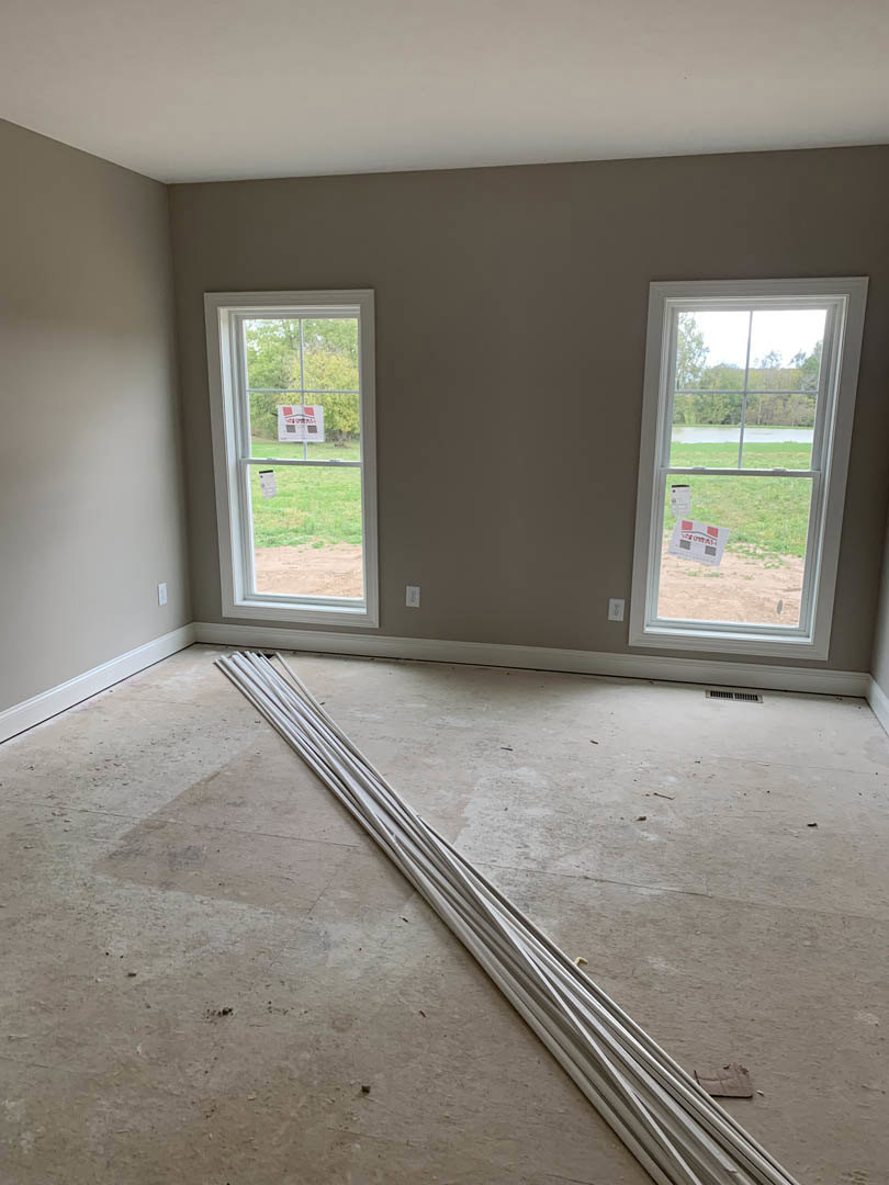 Bright room with smooth white plaster walls, large windows with white frames, white plastic rods scattered on the floor, and a window displaying a sign with red and grey squares