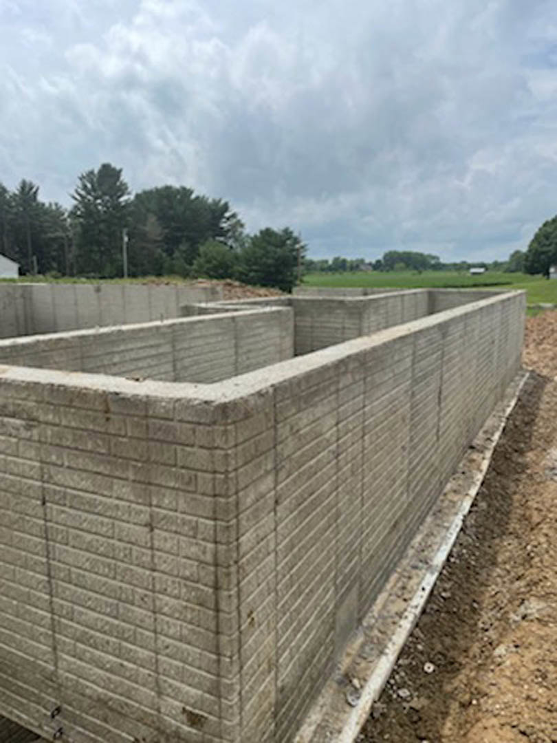 Concrete exterior wall with circular opening, cloudy sky overhead, distant trees visible through the hole