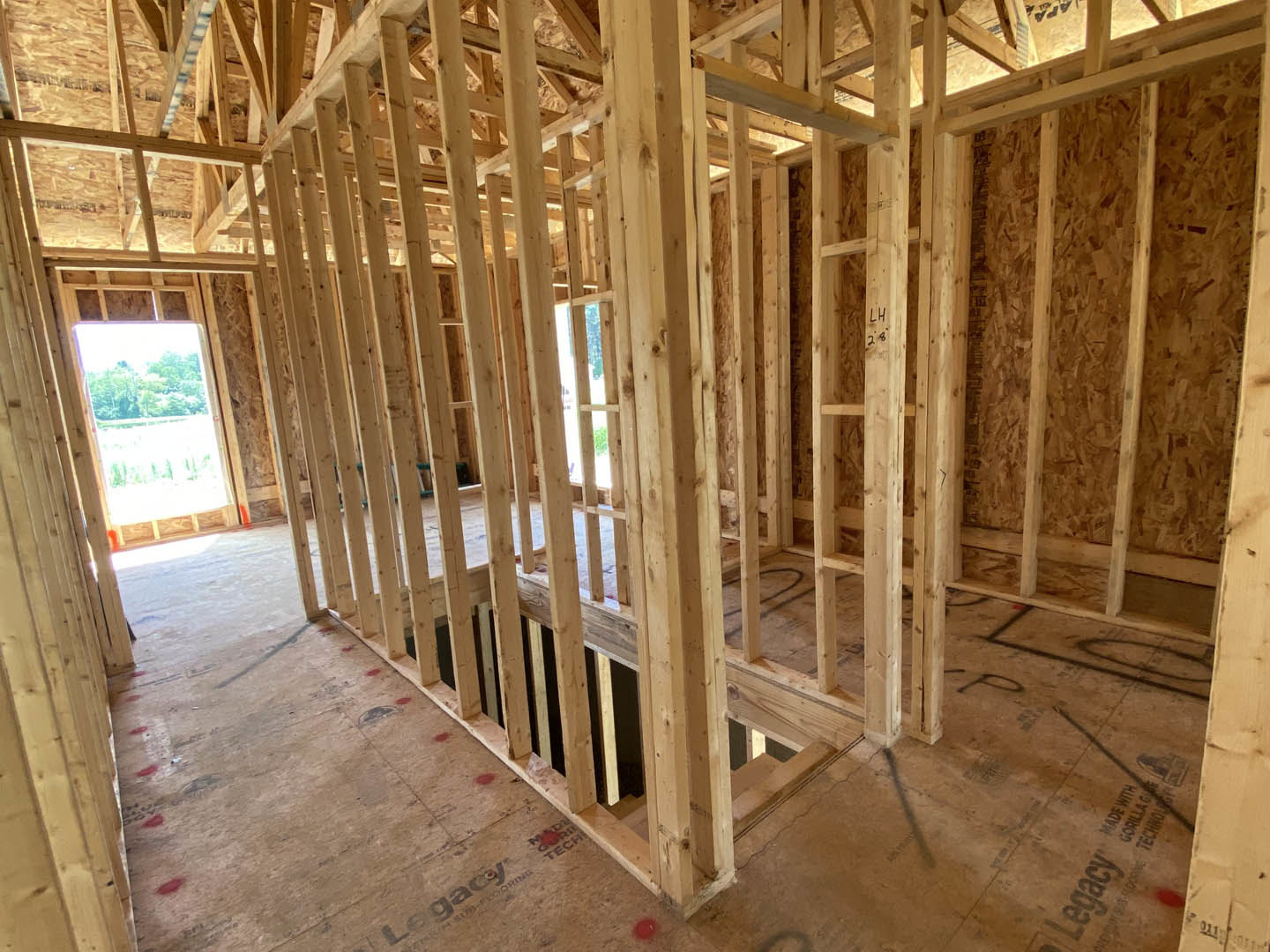 Wood-framed house under construction with exposed beams, unfinished walls, and a window revealing trees outside
