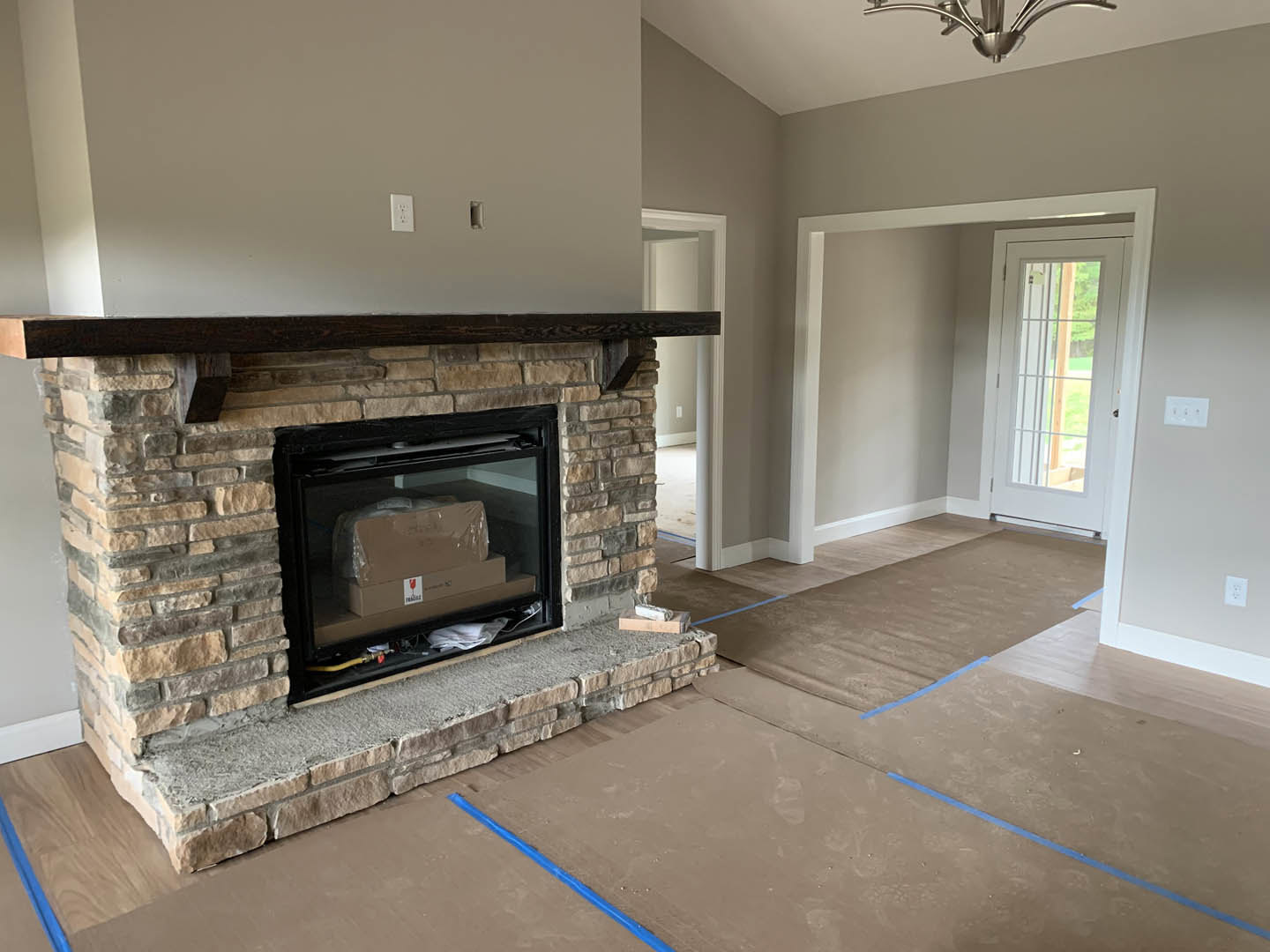 Brick fireplace with black fire screen, wood-burning stove, and brown box on hearth; hardwood flooring and white walls in cozy den.