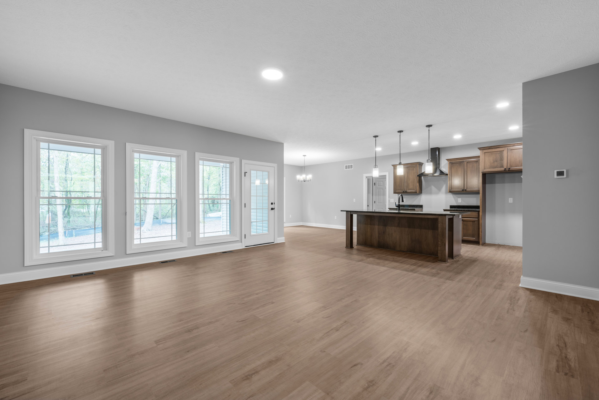 Spacious kitchen with white cabinetry, central island, hardwood flooring, glass-paneled door, large window overlooking trees, and recessed lighting