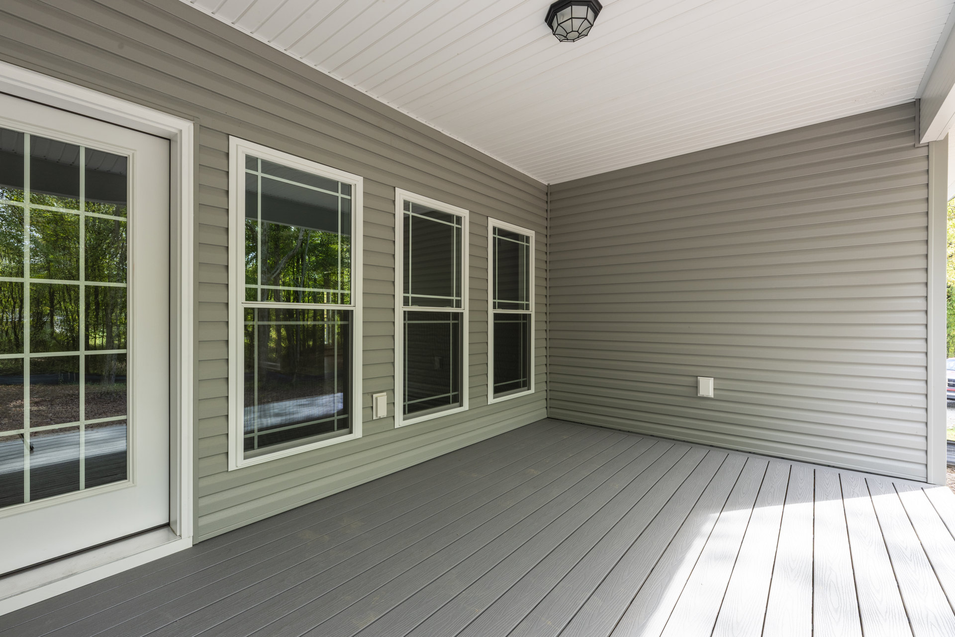 Wood deck with large windows along the side, ceiling-mounted light fixture, and view of trees outside through the glass.