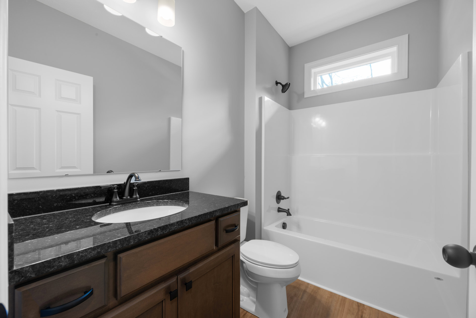 Bathroom with white bathtub, sink set in wood vanity, chrome faucet, white toilet, tiled walls, window letting in natural light, curved shower head