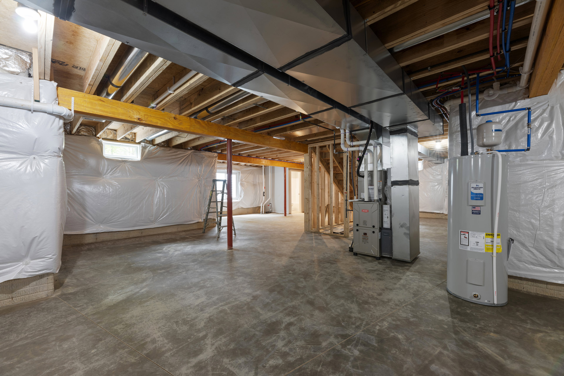 Basement interior with exposed metal ceiling beams, visible pipes, a freestanding ladder, grey utility container, and white plastic wall covering.