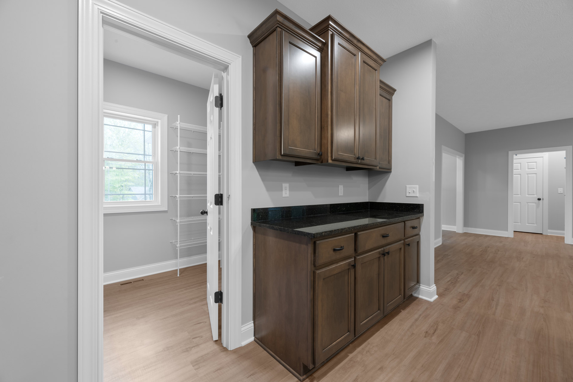 Kitchen with dark wood cabinets, black granite countertop, wood flooring, white-framed window, and white door with black handle