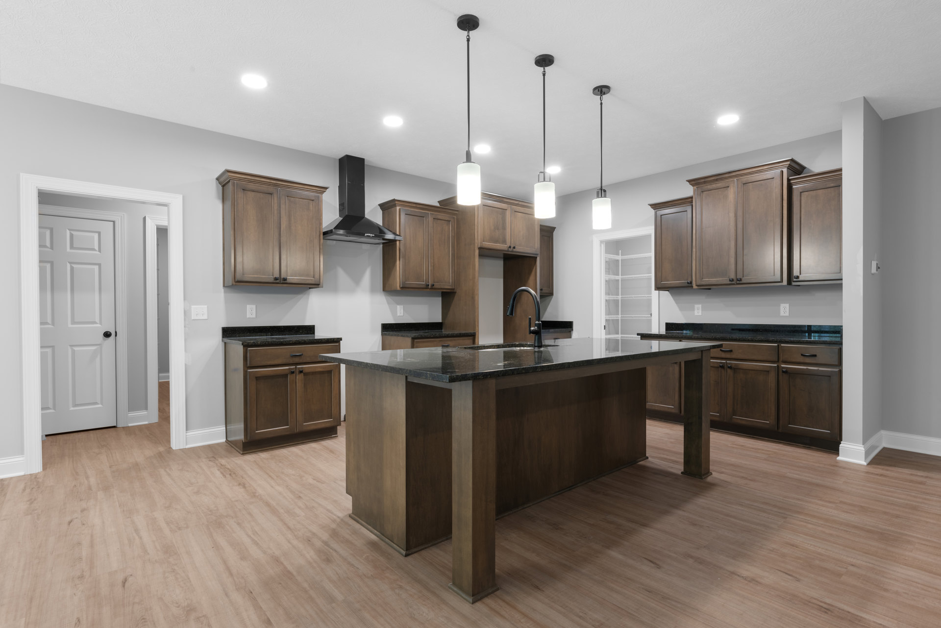 Modern kitchen featuring a central island with black granite countertop, wooden cabinets with black handles, white door with black handle, stainless steel sink, and light-colored