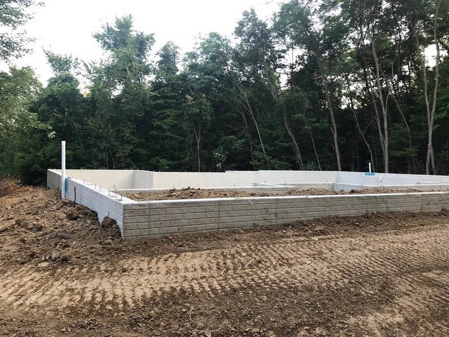 Concrete house foundation surrounded by dirt and soil, bordered by trees and greenery under a clear sky