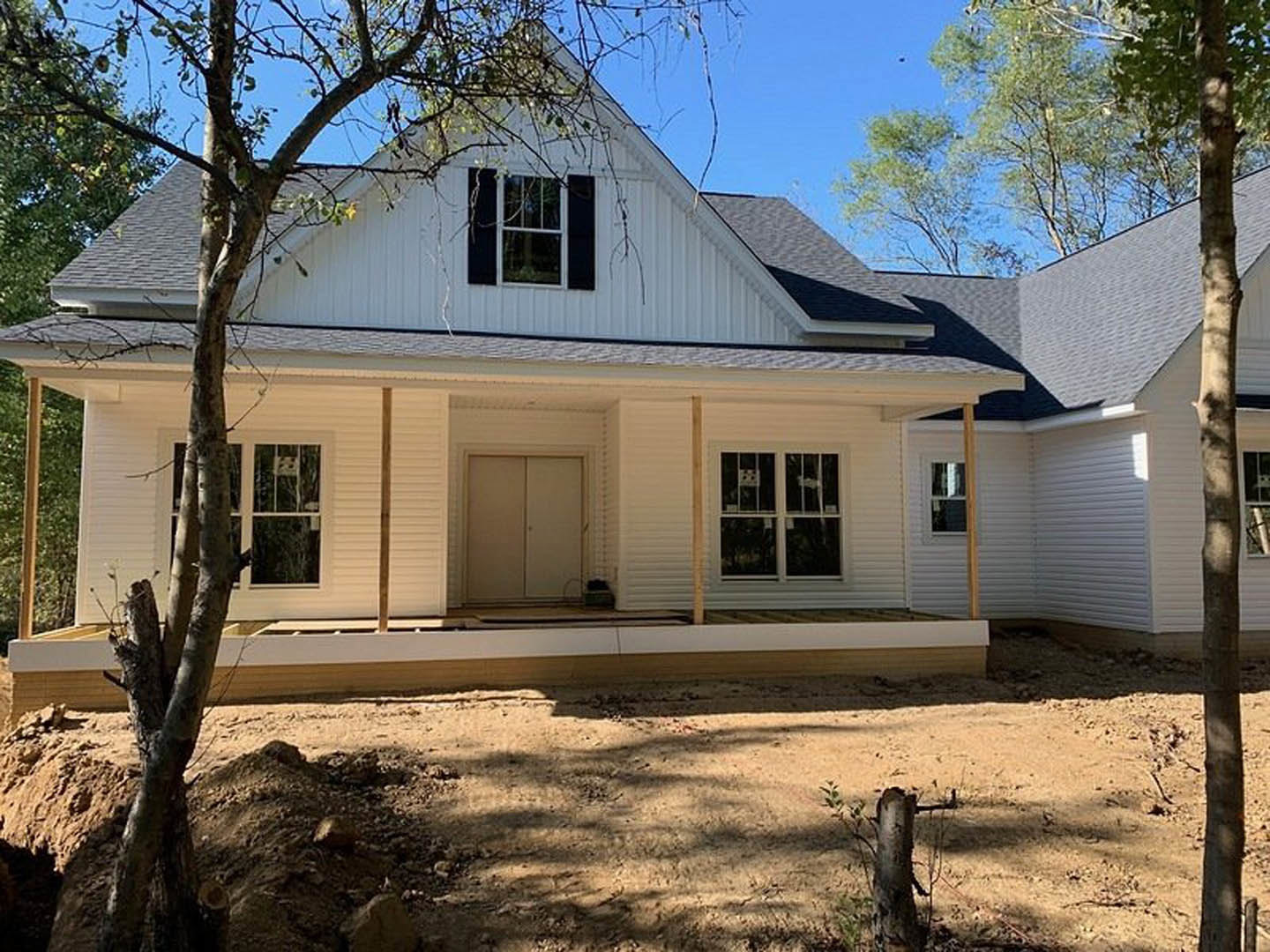 Gray siding house with white trim, covered front porch, large tree in yard, multiple windows, blue sky above