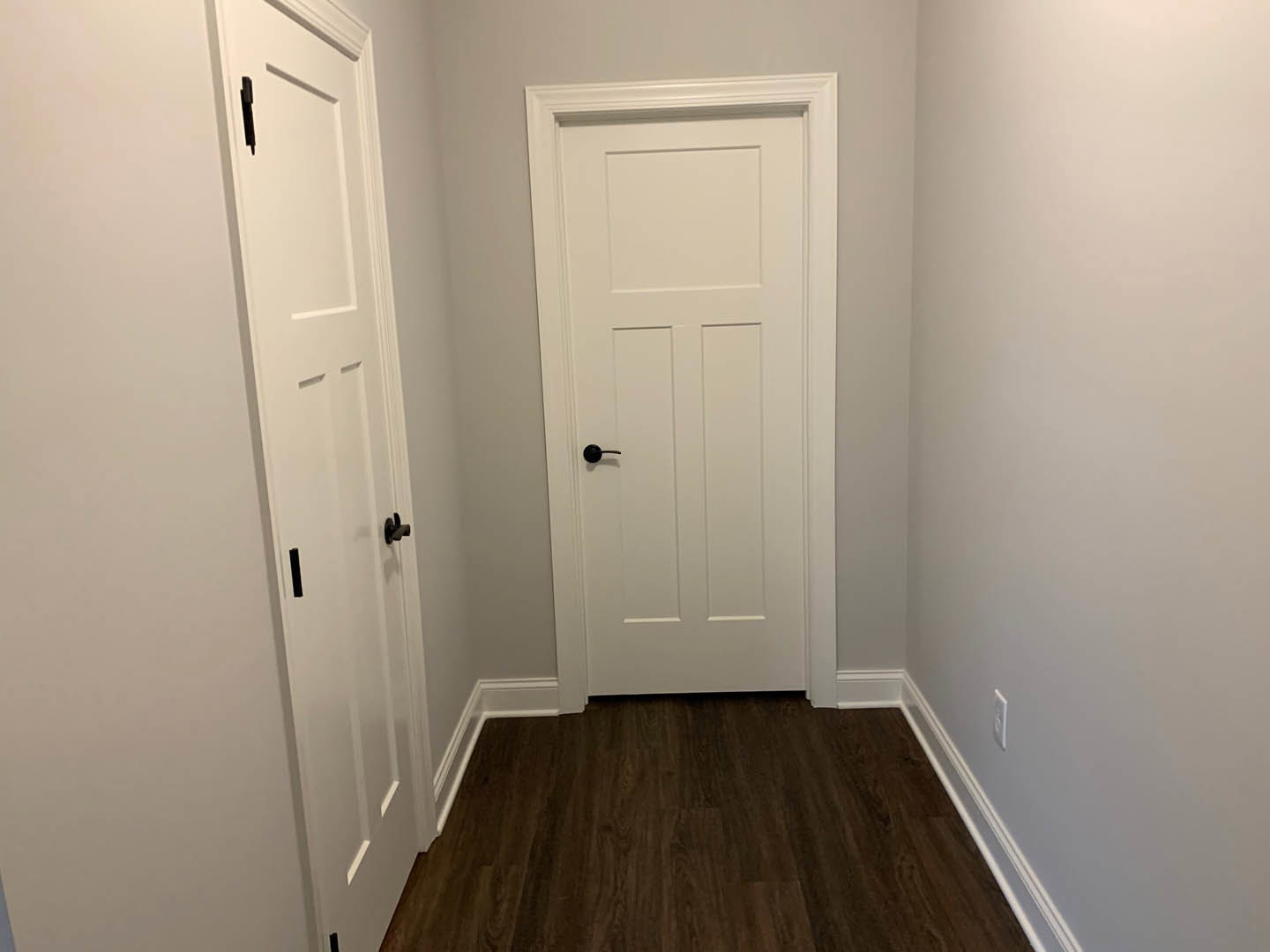 White door with black handle set in a white wall, dark wood flooring, ceiling light fixture visible