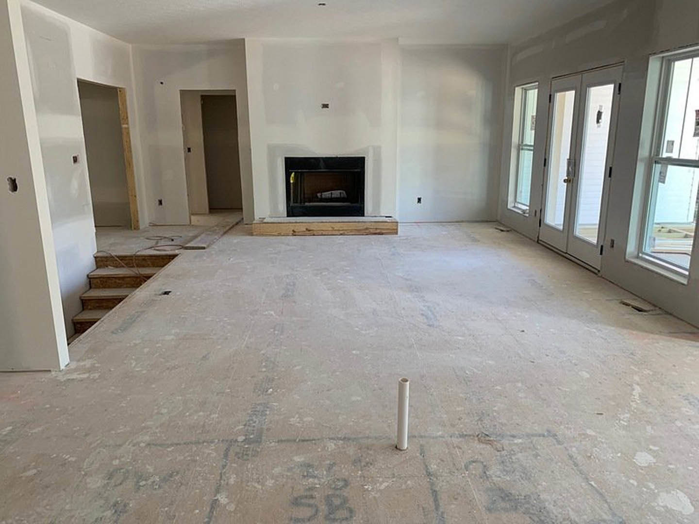 Living room with plaster walls, wood flooring, modern fireplace, staircase with white railing, large window, and a bed visible in an adjacent space.