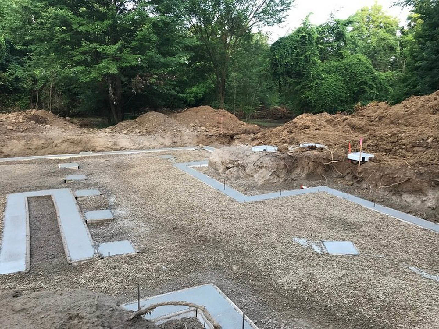 Expansive construction site with exposed soil, scattered concrete slabs, orange cones, and mature trees bordering the area