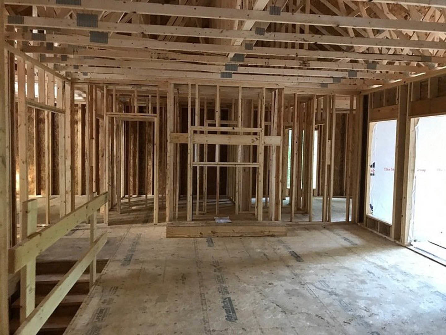 Exposed wood framing with beams and planks, unfinished staircase with wooden railing, close-up of wooden ceiling, taped wood flooring, window detail, white sign with red text.