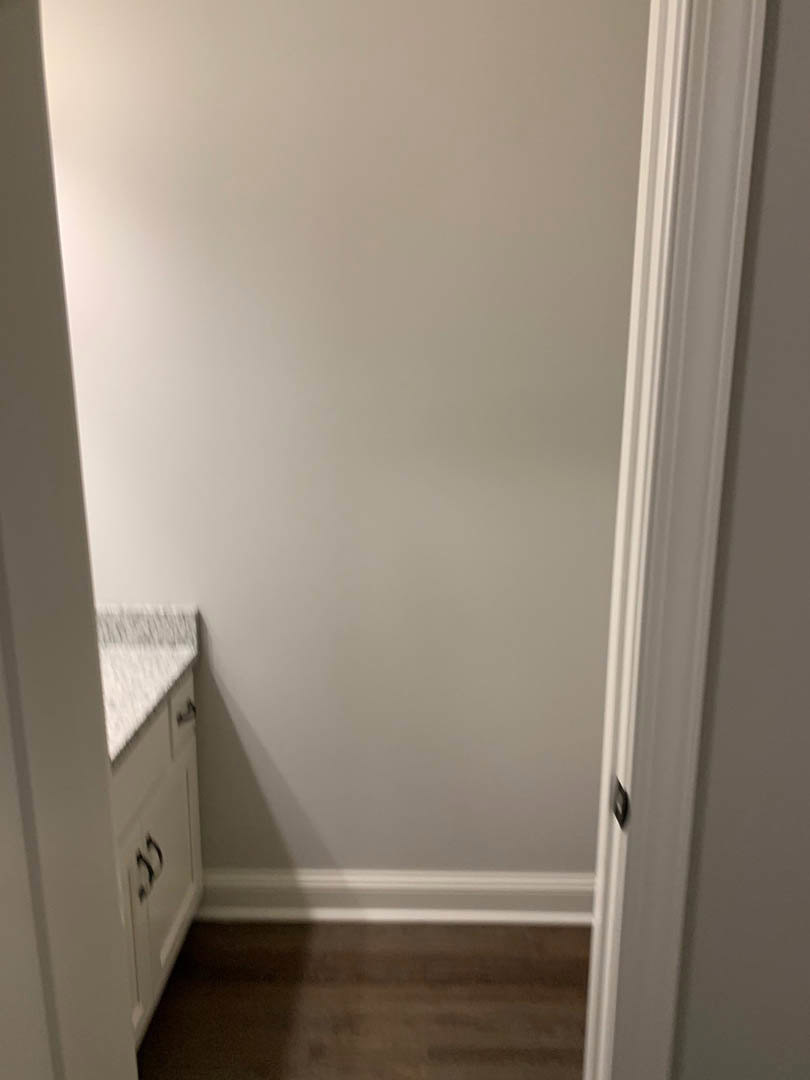 White plaster wall with marble countertop, wood flooring, and door frame visible in foreground