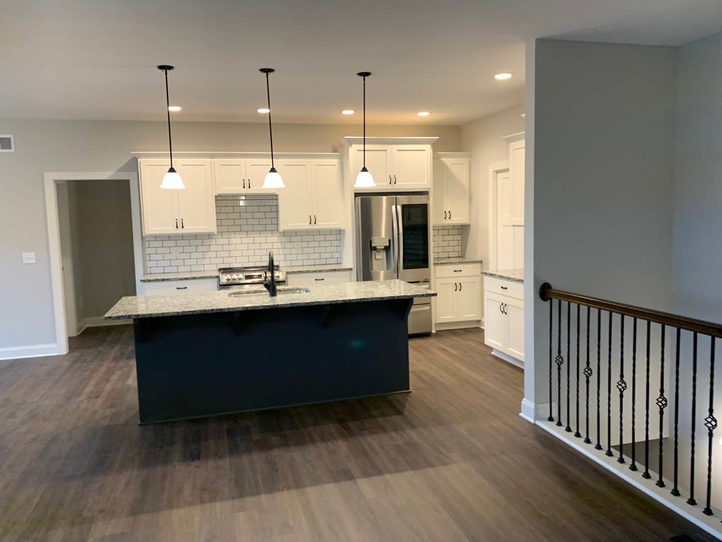 Open kitchen with wood flooring, central island featuring black countertop, stainless steel sink and stove, modern cabinetry, ceiling light fixture, and partial view of railing and