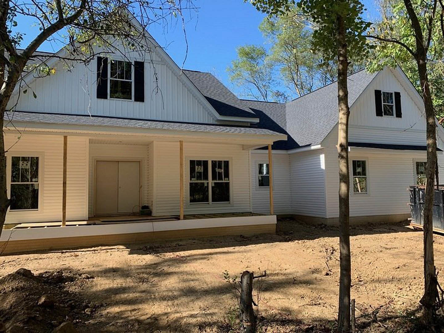Partially built house with exposed wooden framing, white window frames, unfinished siding, and surrounding trees in the background